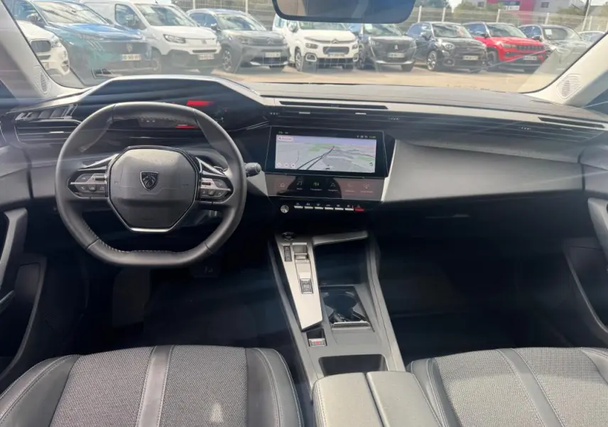 Vue intérieure avant du Peugeot 308 Hybrid gris, avec volant compact, écran tactile central et console moderne.