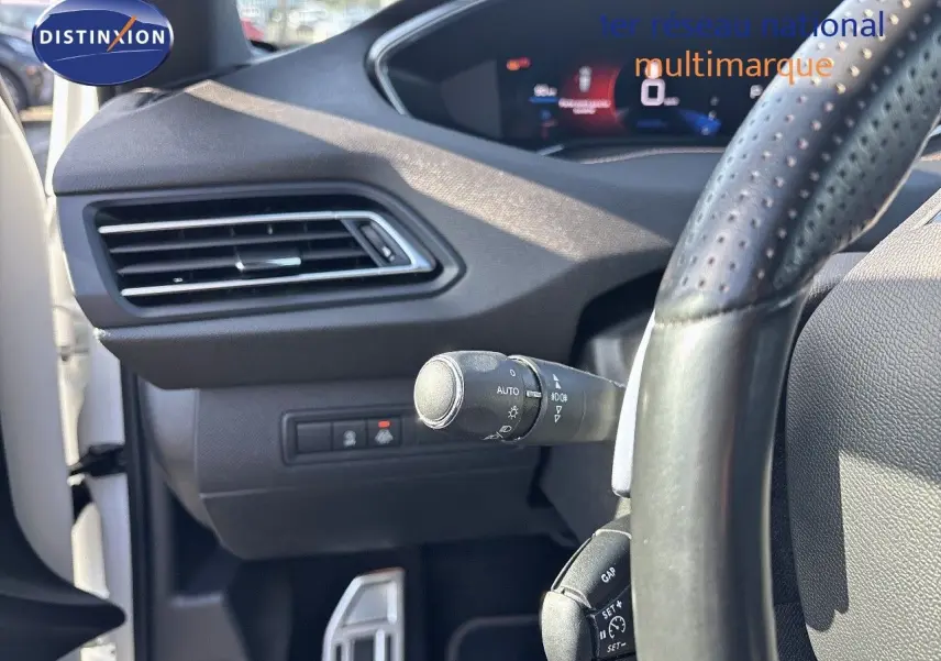 Gros plan sur la partie gauche du tableau de bord et volant perforé d'une Peugeot 308 blanc nacré de 2021.