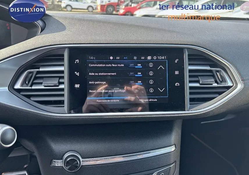 Tableau de bord de Peugeot 308 blanc nacré, écran tactile central affichant les réglages d'aide à la conduite.