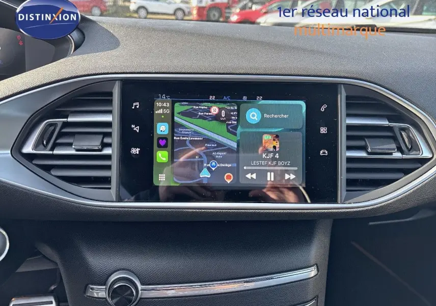 Écran tactile central avec navigation et musique dans l'habitacle d'une Peugeot 308 blanche nacrée, vue de face.