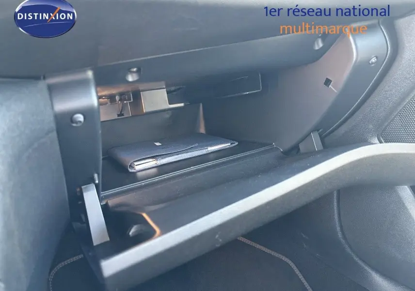 Gros plan sur la boîte à gants ouverte du Peugeot 308 blanc nacré, montrant un carnet à l'intérieur.