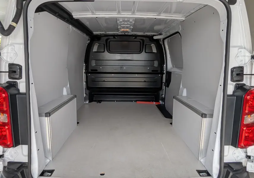 Vue arrière du fourgon blanc Peugeot Expert M 180 EAT8 montrant l’espace de chargement avec plancher bois antidérapant.