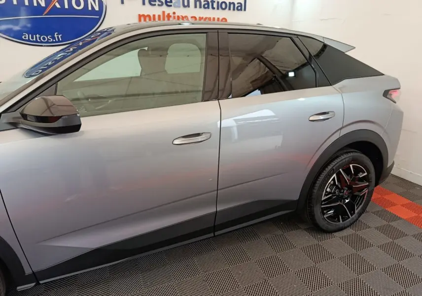 Profil côté gauche du Peugeot 3008 gris clair 2025 avec jantes noires et vitres teintées dans un showroom.