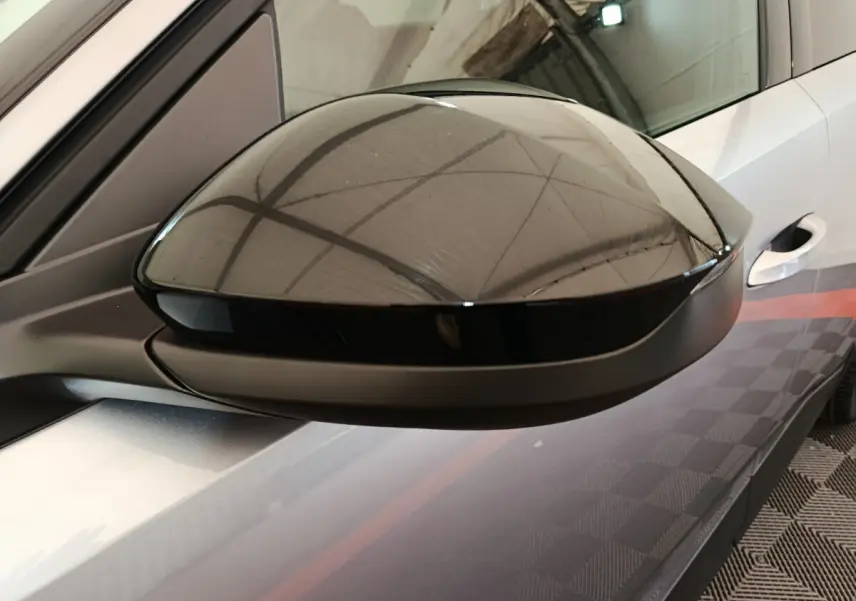 Rétroviseur côté gauche noir brillant sur Peugeot 3008 gris clair, avec reflet de l'environnement intérieur.