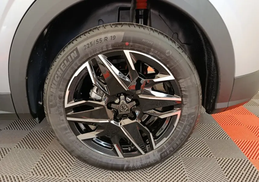 Gros plan sur la roue avant droite du Peugeot 3008 gris clair 1.2 HYBRID 145 E-DCS6 GT avec jante noire et chromée.