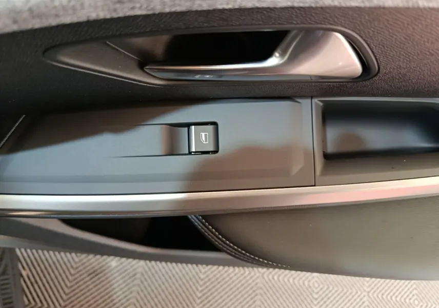 Poignée de porte intérieure côté gauche avec bouton de commande de vitre sur Peugeot 3008 gris clair 2025.