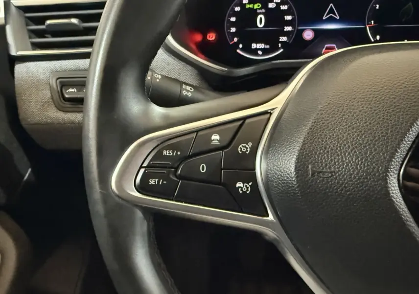 Gros plan sur le volant noir de la Renault Clio 2024 avec commandes de régulateur de vitesse et tableau de bord numérique.