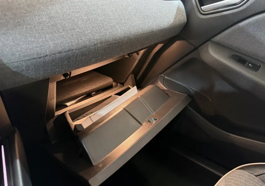 Gros plan de la boîte à gants ouverte côté passager dans l'habitacle sombre d'une Renault Clio rouge 2024.