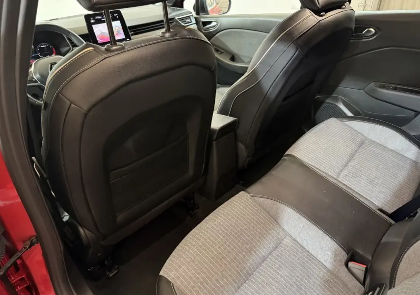 Vue intérieure arrière droite de la Renault Clio rouge 2024, sièges tissu gris et noir avec appuis-tête et écran tactile avant.