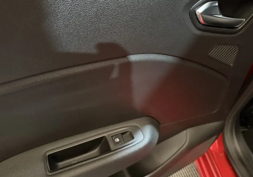 Vue rapprochée de la porte avant gauche rouge d’une Renault Clio 2024 avec commande de lève-vitre électrique.