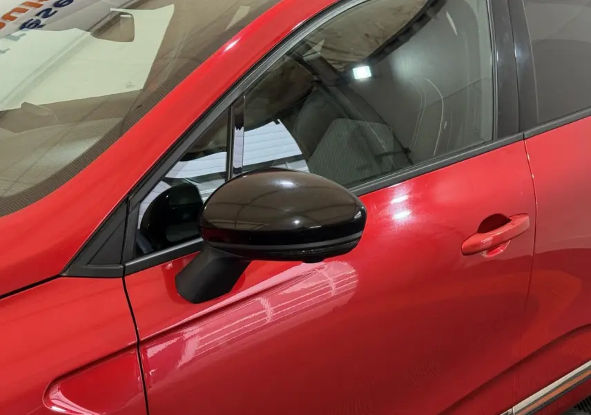 Vue rapprochée du côté gauche d’une Renault Clio Techno TCe 90 rouge, avec rétroviseur noir brillant et poignée de porte assortie.
