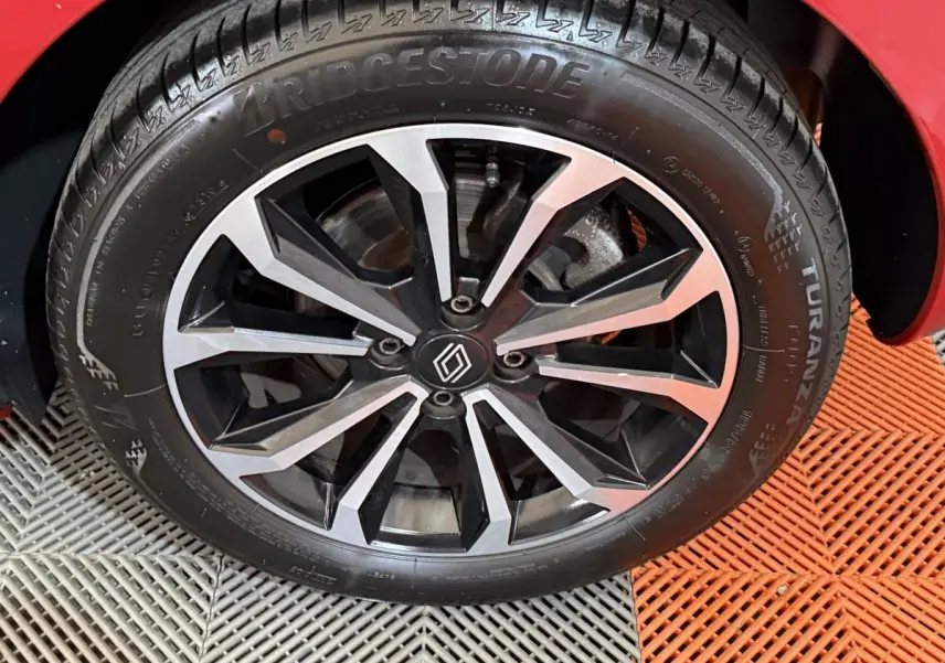 Gros plan sur la roue avant droite d'une Renault Clio rouge 2024 avec jante alliage noire et argentée au design moderne.