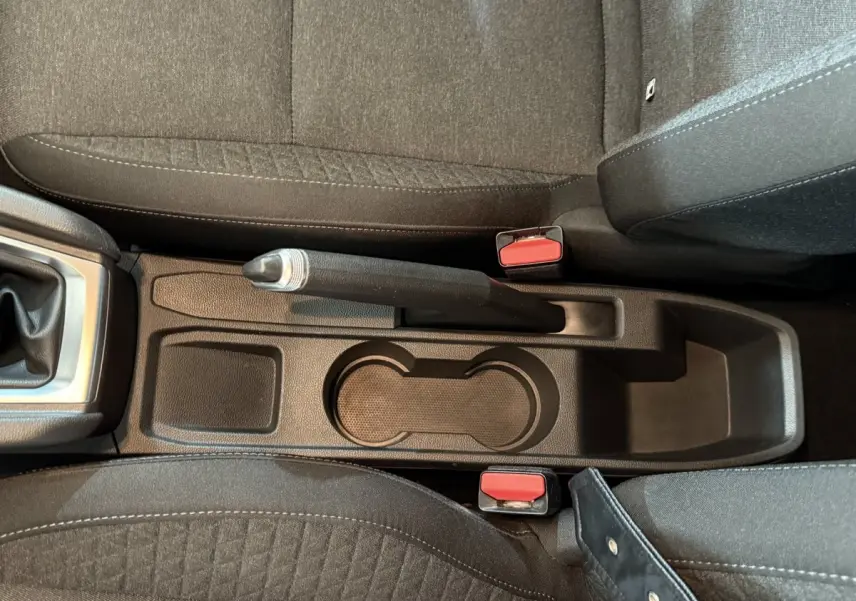 Vue plongeante sur la console centrale noire de la Renault Clio Business blanche, avec frein à main manuel et porte-gobelets.