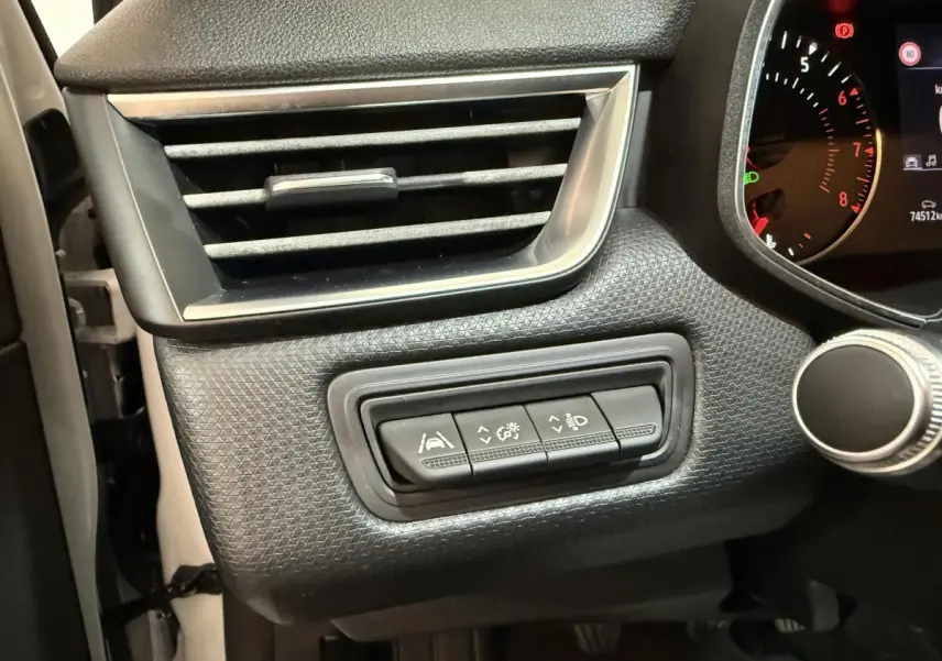 Gros plan sur les commandes d’assistance et réglage des phares à gauche du tableau de bord d’une Renault Clio Business blanche.