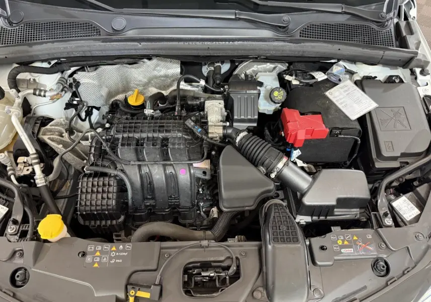 Vue plongeante sur le moteur essence d'une Renault Clio Business blanche de 2021 avec batterie et durites visibles.