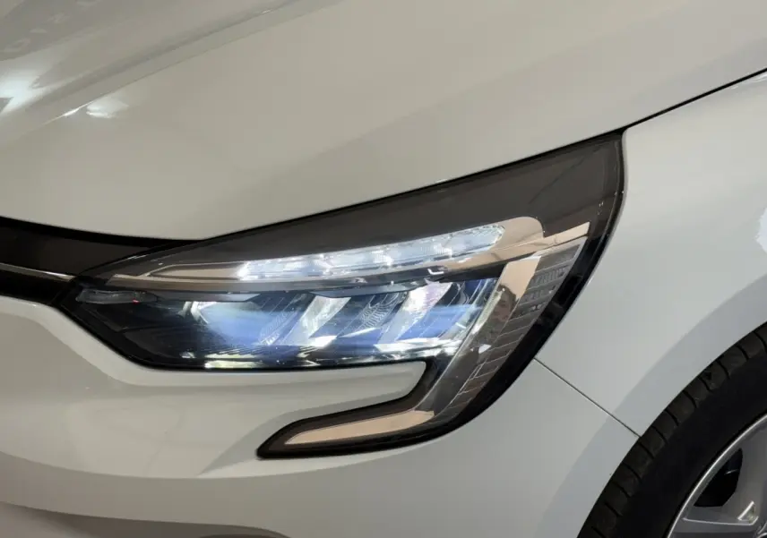 Gros plan sur le phare avant droit blanc d'une Renault Clio Business 2021, mettant en valeur les LED et la carrosserie lisse.