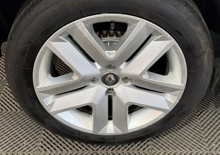 Pneu de secours noir monté dans le coffre d'une Renault Clio Business blanche, vue rapprochée du caoutchouc.