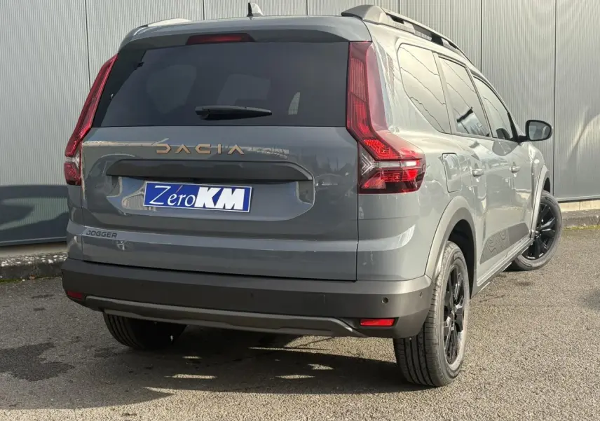 Vue 3/4 arrière droite d'un Dacia Jogger Gris Urbain avec jantes noires et barres de toit longitudinales.
