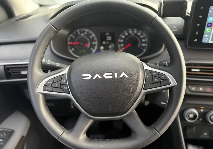 Vue rapprochée du volant noir du Dacia Jogger 2024 avec commandes intégrées et tableau de bord en arrière-plan.