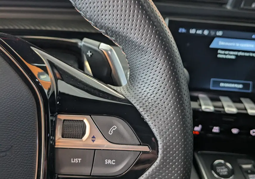 Gros plan sur le volant cuir perforé côté gauche du Peugeot 508 SW gris Selenium avec commandes intégrées et tableau de bord numérique.