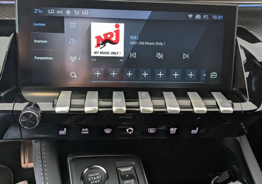 Tableau de bord noir de Peugeot 508 SW 2024 avec écran tactile affichant la radio NRJ et commandes modernes.