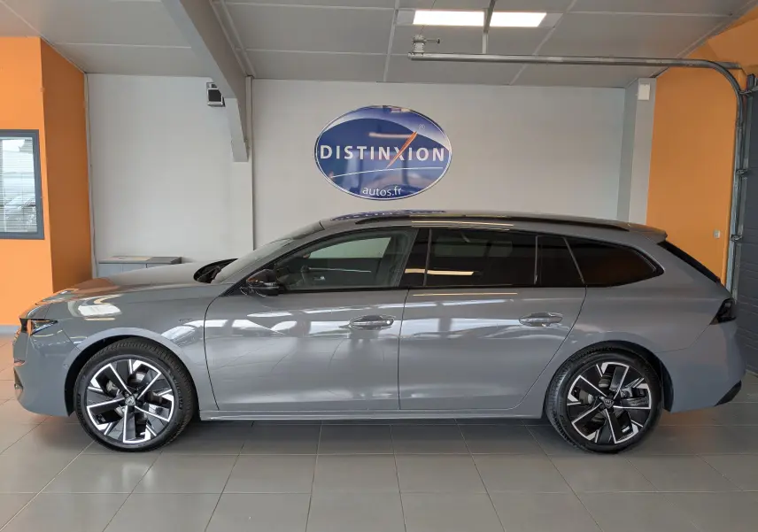 Profil côté gauche d'une Peugeot 508 SW gris selenium 2024 avec jantes alliage et vitres arrière surteintées en intérieur showroom.