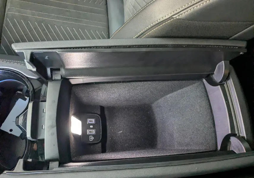 Vue plongeante sur le rangement central ouvert de la Peugeot 508 SW gris selenium, avec ports USB visibles et intérieur noir.