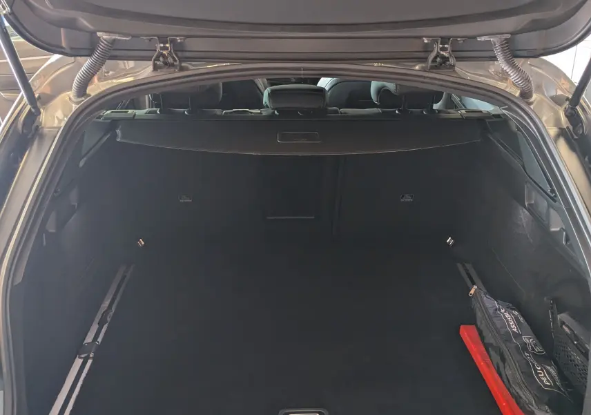 Coffre ouvert vu de l'arrière d'une Peugeot 508 SW gris selenium, avec tapis noir et kit de sécurité rangé à droite.