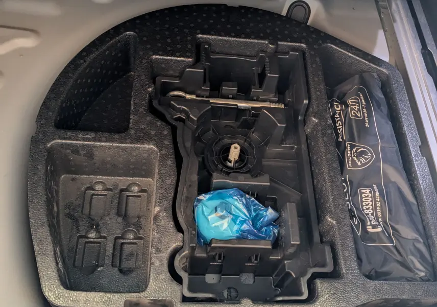 Compartiment de rangement sous le coffre du Peugeot 508 SW gris Selenium, montrant l'emplacement pour roue de secours et kit d'assistance.