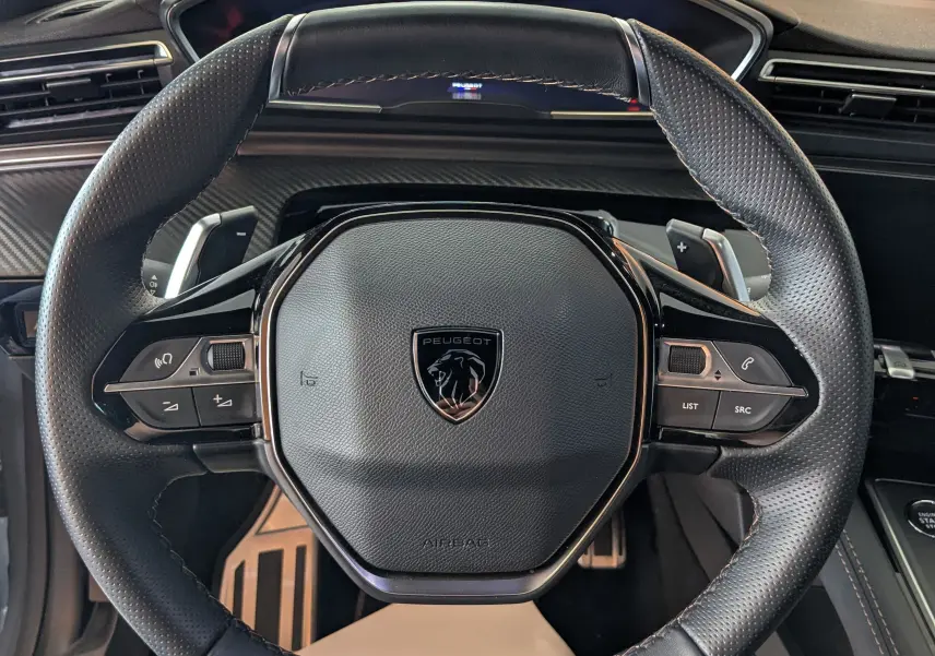 Volant cuir perforé avec logo Peugeot et inscription GT, vue rapprochée de l'intérieur du Peugeot 508 SW 2024 gris selenium