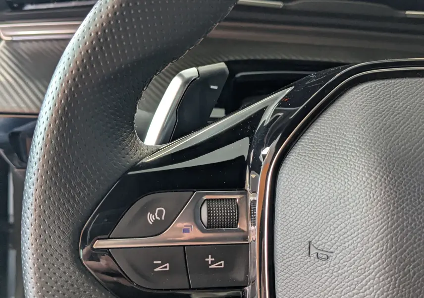 Gros plan sur le volant cuir perforé et les commandes intégrées du tableau de bord d'une Peugeot 508 SW 2024.