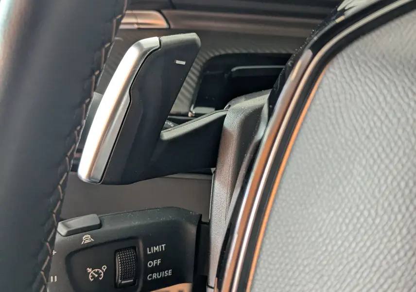 Gros plan sur la commande de régulateur de vitesse et levier de boîte automatique dans le volant cuir noir du Peugeot 508 SW gris selenium.