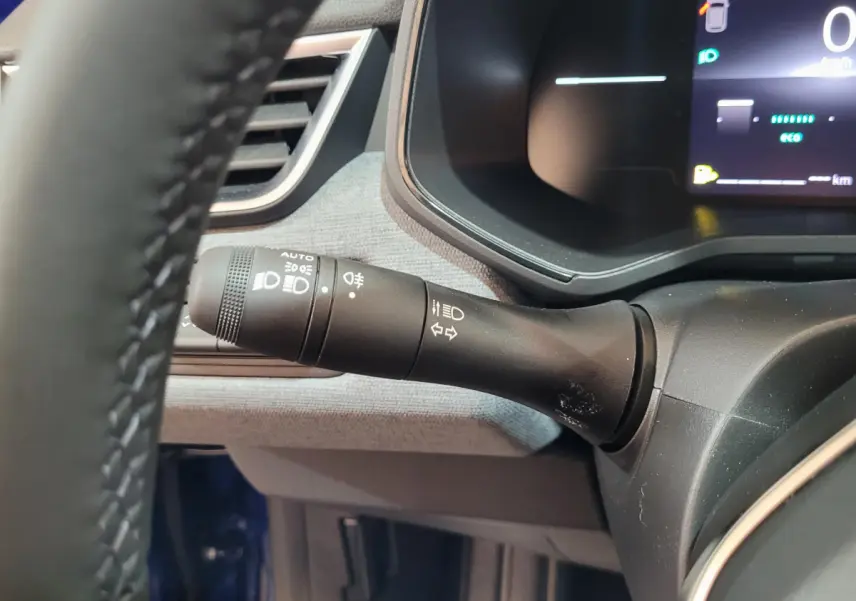 Gros plan sur la commande des phares à gauche du volant dans l'habitacle bleu d'une Renault Clio 2025.