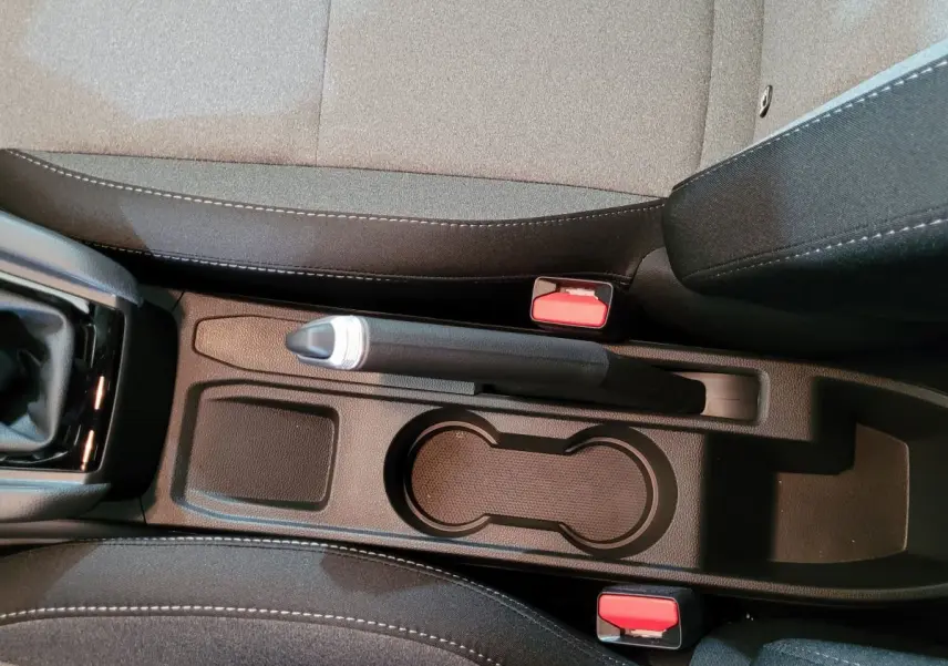 Vue plongeante sur la console centrale noire de la Renault Clio bleu, avec frein à main manuel et porte-gobelets.