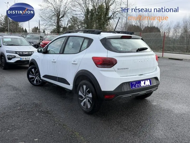 Vue 3/4 arrière droite d'une Dacia Sandero 2025 blanche Glacier avec jantes noires et détails noirs contrastants.