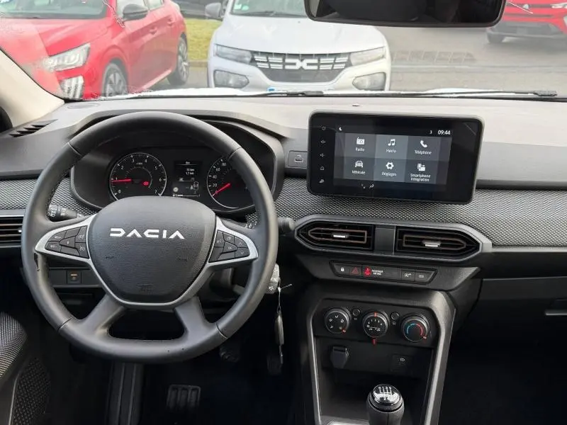 Vue intérieure de face du tableau de bord d'une Dacia Sandero blanche 2025, avec volant multifonction et écran tactile central.