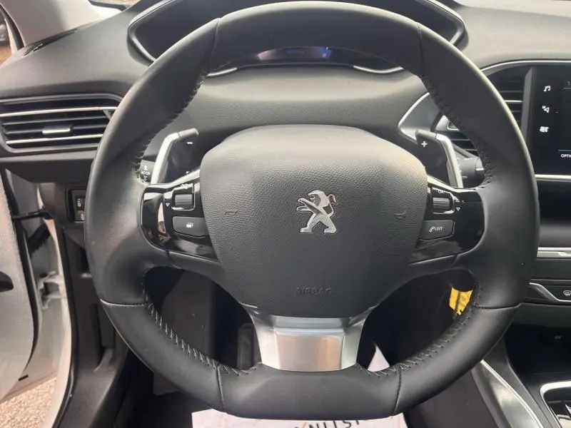 Vue rapprochée du volant cuir multifonction noir de la Peugeot 308, avec tableau de bord et écran tactile visibles.