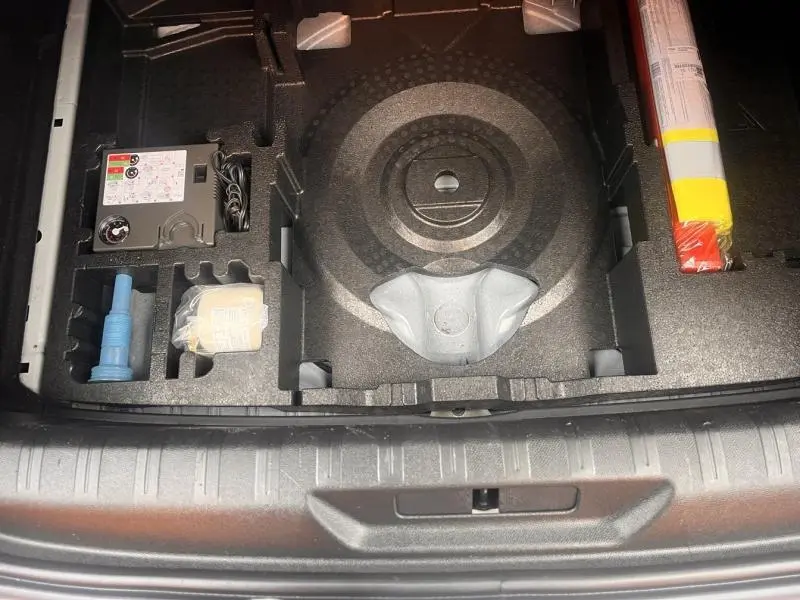 Vue rapprochée du coffre ouvert d'une Peugeot 308 blanc Banquise, montrant le rangement sous la moquette avec kit de réparation pneus.
