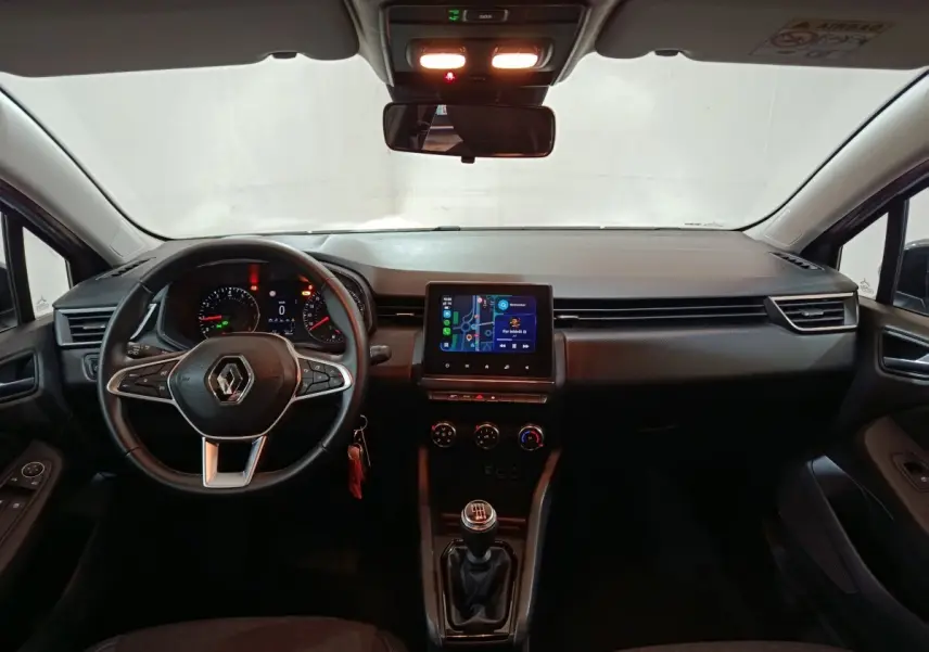 Vue intérieure avant de la Renault Clio gris clair 2023, volant multifonctions cuir et écran tactile central allumé.