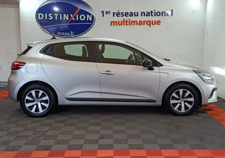 Profil droit d'une Renault Clio gris clair 2023 avec jantes alliage et rétroviseurs noirs dans un showroom.