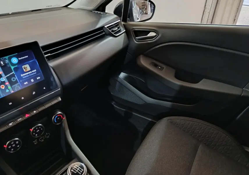 Vue intérieure côté passager de la Renault Clio 2023 gris clair, avec tableau de bord et écran tactile central.