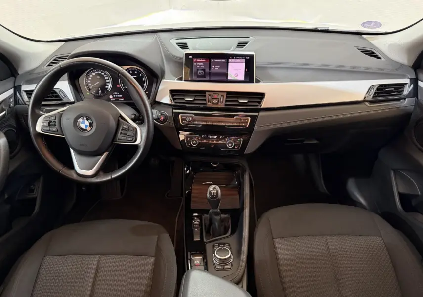 Vue intérieure avant du BMW X2 sDrive18i Lounge 2023, tableau de bord noir avec écran central et volant cuir multifonctions.