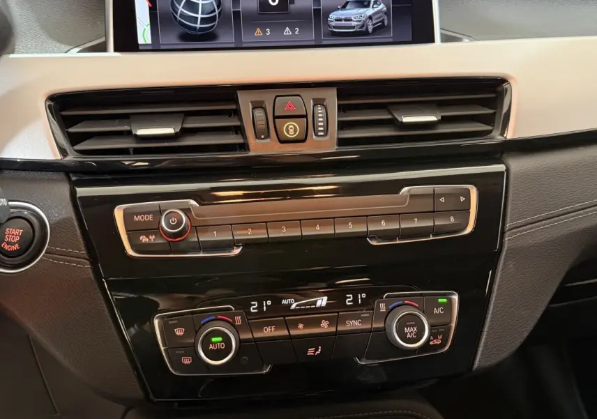 Vue rapprochée du tableau de bord noir et beige du BMW X2 sDrive18i Lounge 2023 avec commandes climatisation et écran central.