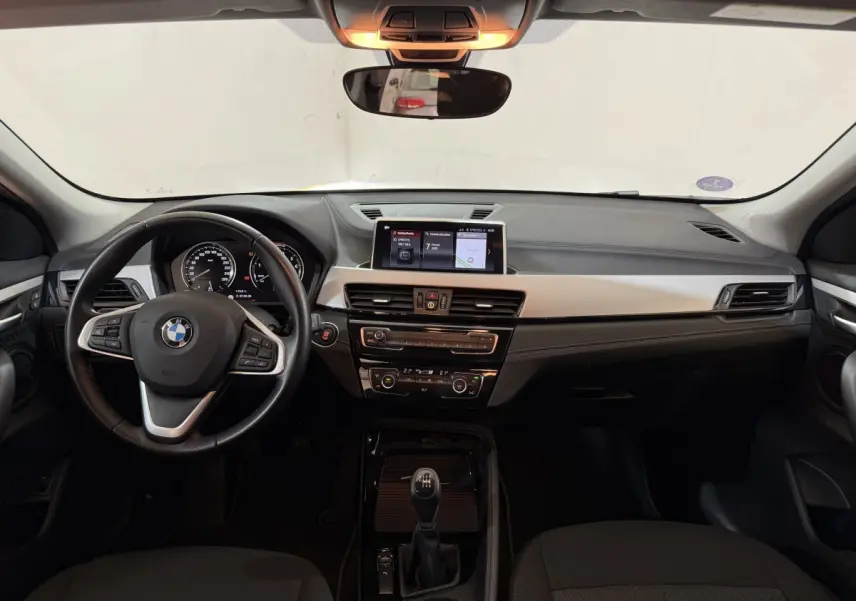 Vue frontale de l'intérieur du BMW X2 sDrive18i Lounge 2023, tableau de bord noir avec écran central et volant cuir.