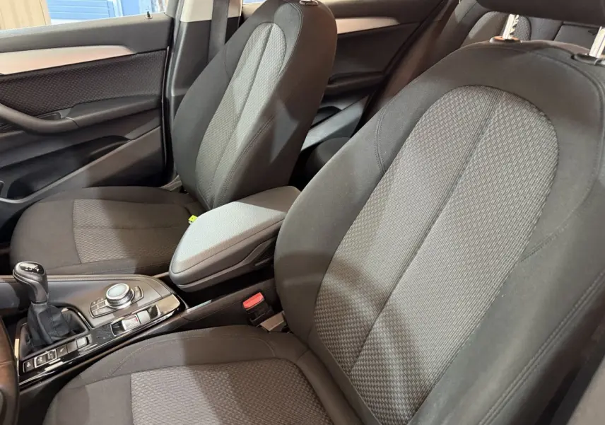 Vue intérieure rapprochée des sièges avant tissu gris et console centrale avec levier de vitesses manuelle d'une BMW X2.