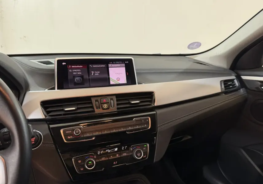 Vue intérieure du tableau de bord de la BMW X2 sDrive18i Lounge 2023 avec écran central et commandes climatisation.