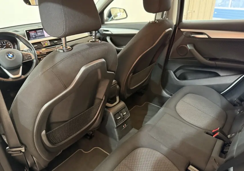 Vue intérieure arrière côté droit de la BMW X2 sDrive18i Lounge 2023 avec sièges tissu noirs et console centrale.