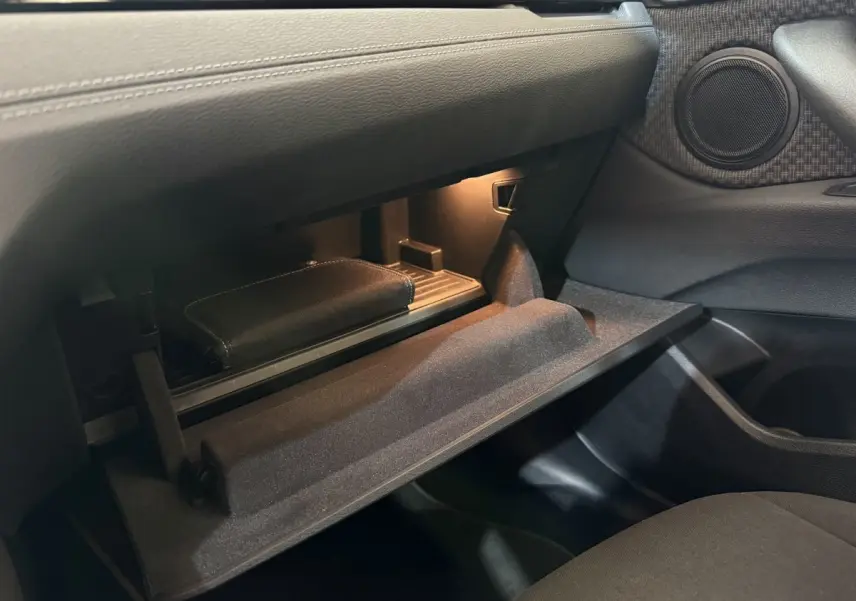 Vue intérieure du vide-poche passager ouvert d'une BMW X2 sDrive18i Lounge 2023, avec éclairage intérieur doux.