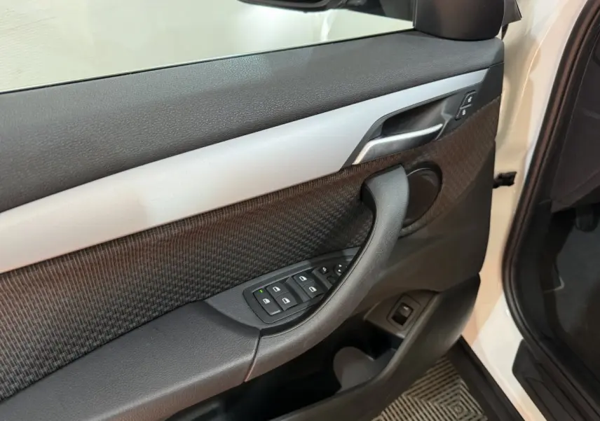 Vue rapprochée de la porte avant gauche blanche du BMW X2 sDrive18i Lounge, avec commandes des vitres et poignée noire.