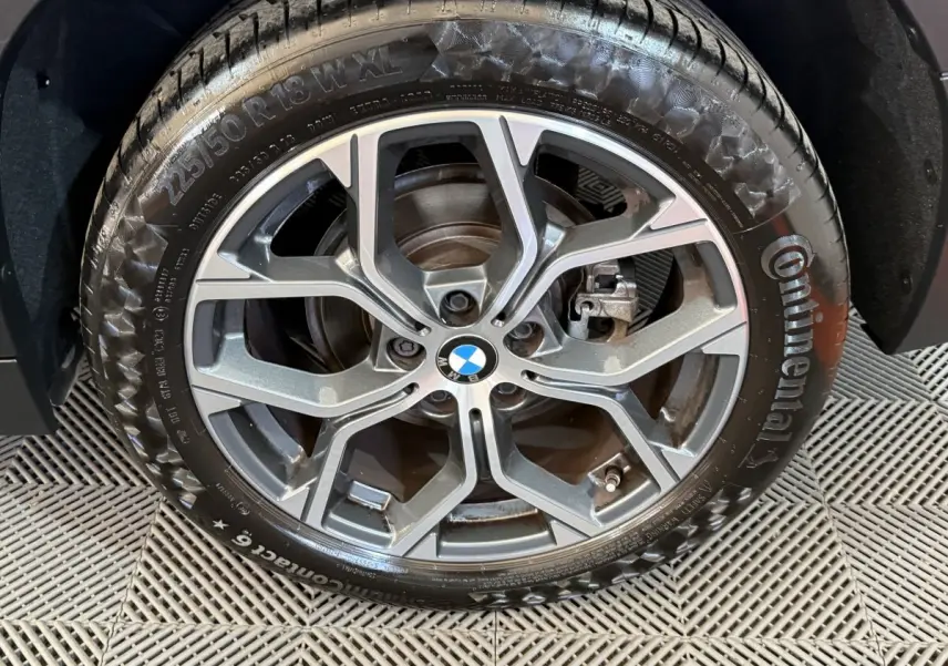 Gros plan sur la roue avant droite d’une BMW X2 blanche 2023, avec jante alliage à design moderne et logo BMW central.